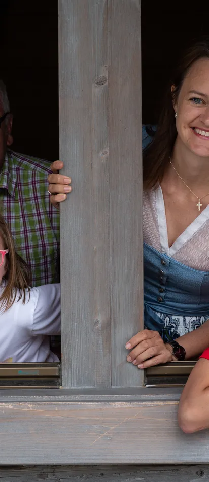Lächelnde Mehrgenerationenfamilie schaut aus einem Holzfenster einer Hütte